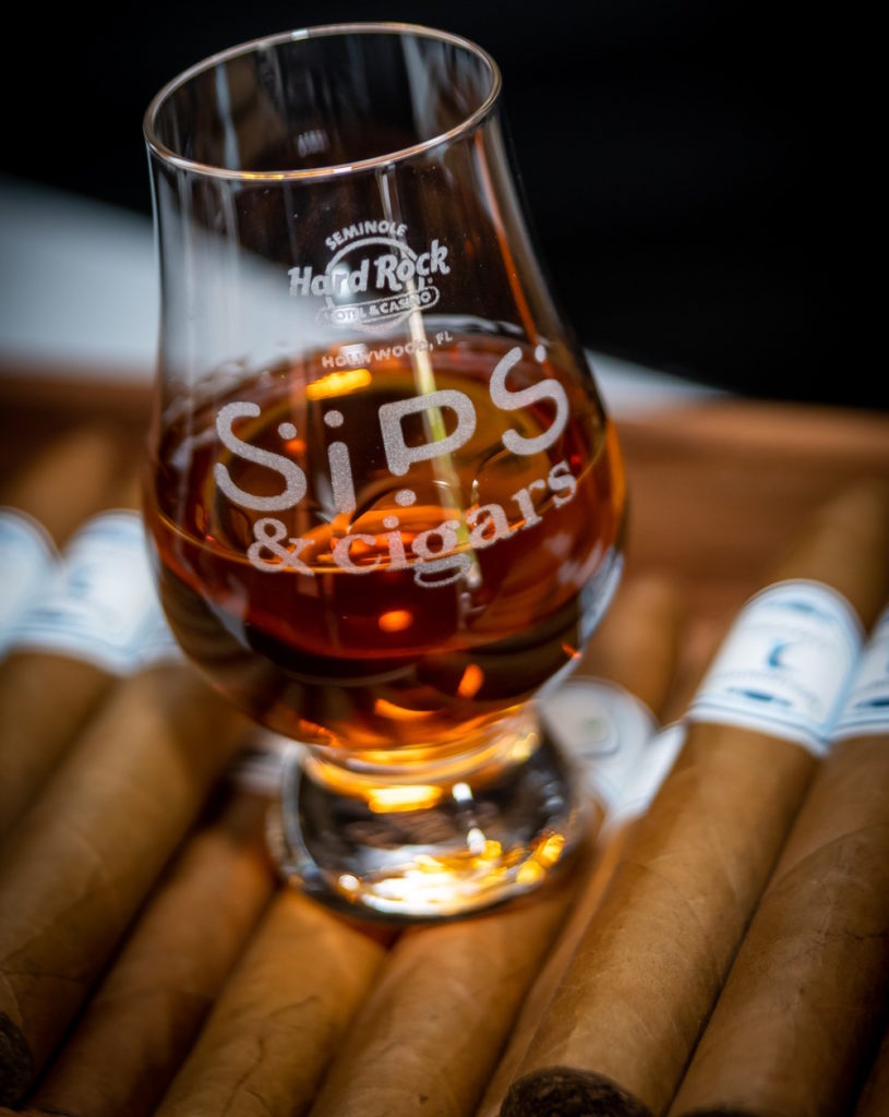 A Glencairn glass of whiskey atop a box of handrolled cigars.